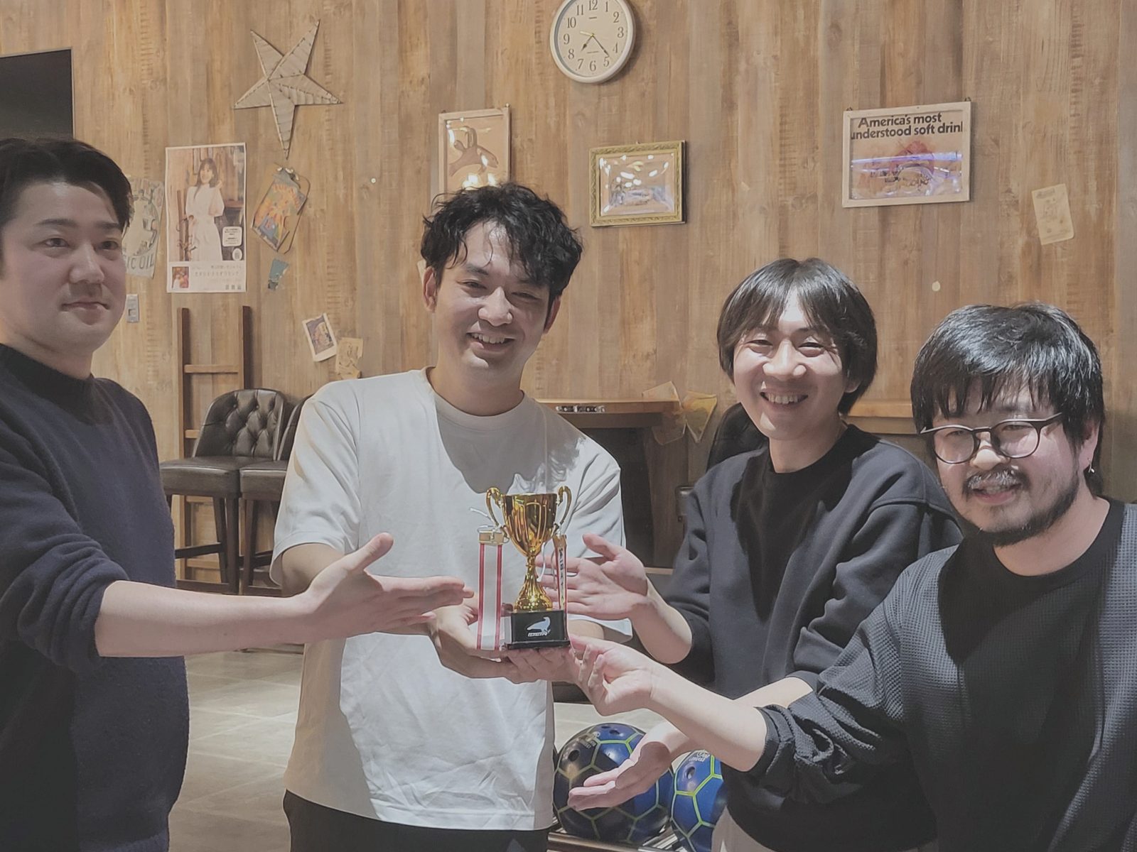 優勝トロフィーとボウリングの球を手に笑顔で並ぶ社員たち